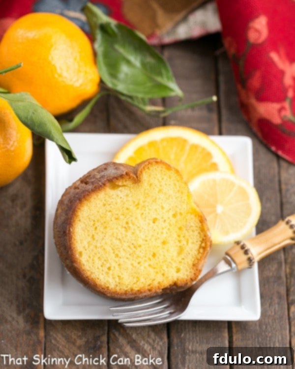 A perfectly sliced Easy Lemon Bundt Cake on a square white plate, garnished with fresh lemon and orange slices, highlighting its moist texture and golden hue.