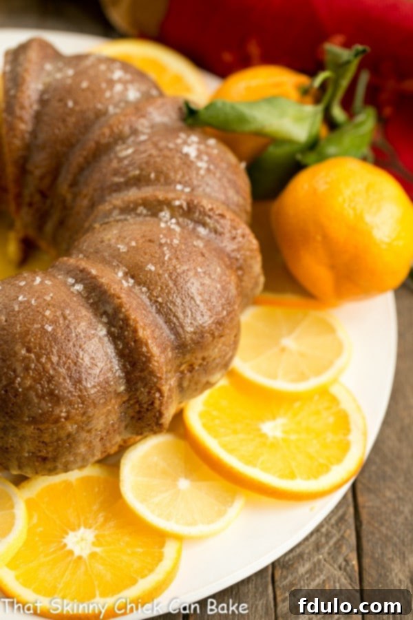 A beautifully decorated Easy Lemon Bundt Cake on a white cake plate, surrounded by fresh lemon and orange slices for a vibrant presentation.