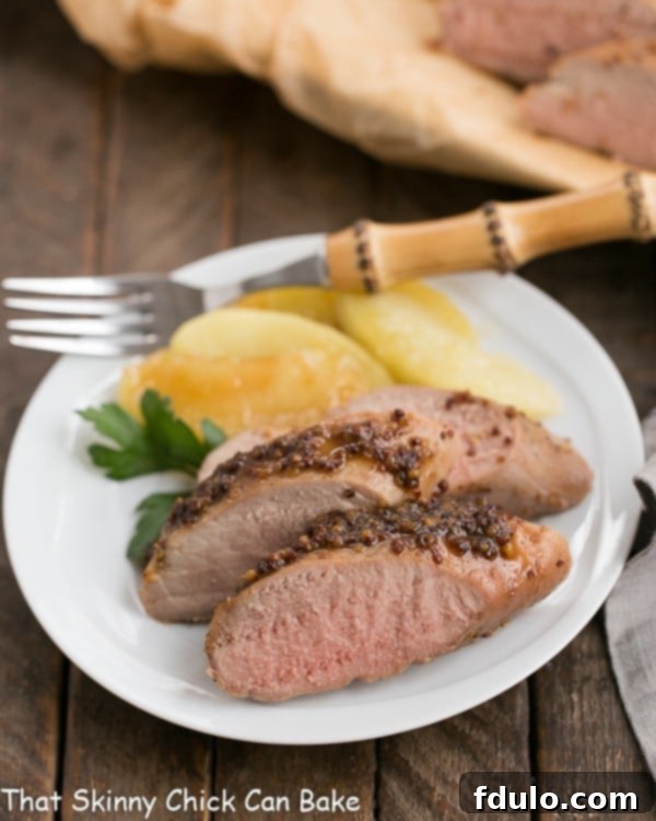 A plate of sliced apple mustard pork tenderloin with a bamboo handle fork.