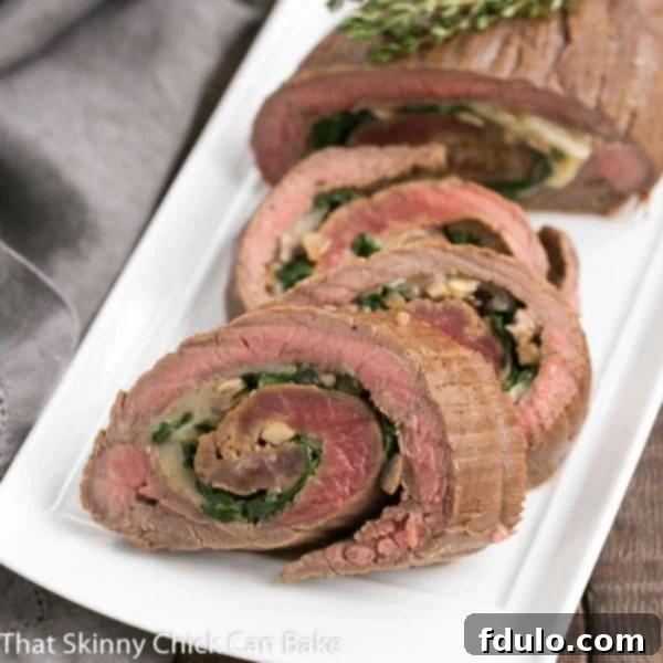 Perfectly cooked Flank Steak Roulades resting on a white rectangular tray, ready to be sliced and served. The golden-brown crust hints at the tender, flavorful interior filled with vibrant spinach, mushrooms, and melted Provolone cheese.