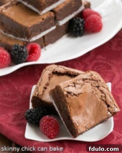 2 fudgy brownies on a white ceramic plate with 2 berries.