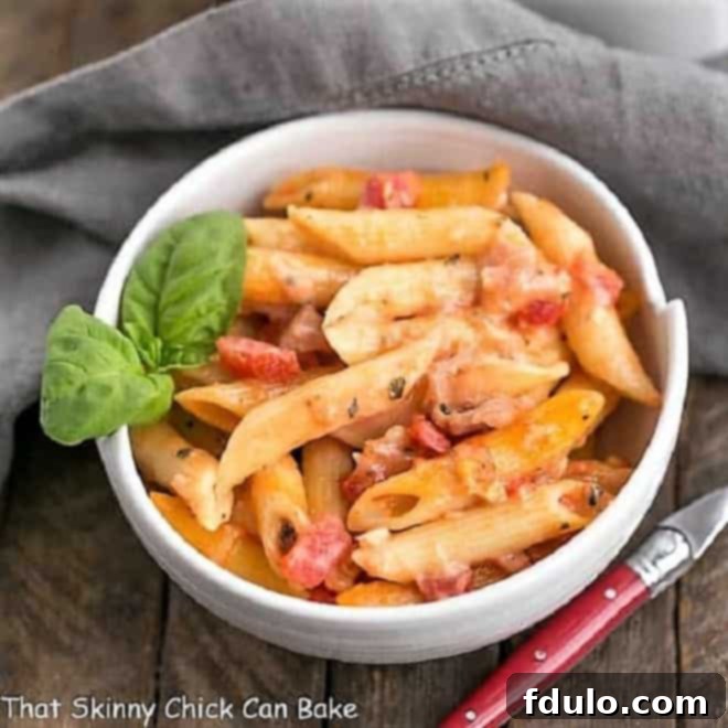 An overhead shot of Cheesy Baked Pasta in a pristine white bowl, adorned with a fresh sprig of basil, highlighting its rich, creamy texture and inviting presentation.