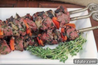 Close-up of grilled Greek kabobs on a white tray, garnished with fresh thyme.