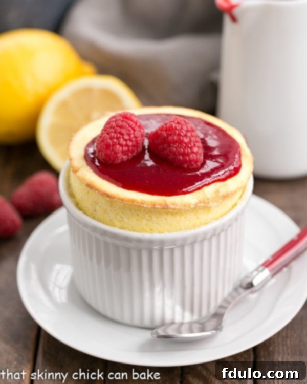 Delightful Raspberry Topped Lemon Soufflés served in a white ramekin on a saucer with a red handled spoon, ready to be enjoyed.