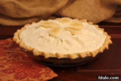 Close-up view of a whole Banana Cream Pie, rich cream filling and a perfect golden-brown crust, presented next to a vibrant orange napkin.