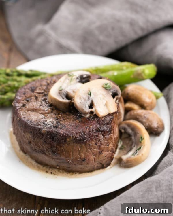 Mushroom Topped Pepper Steak topped with mushrooms on a white plate with asparagus spears