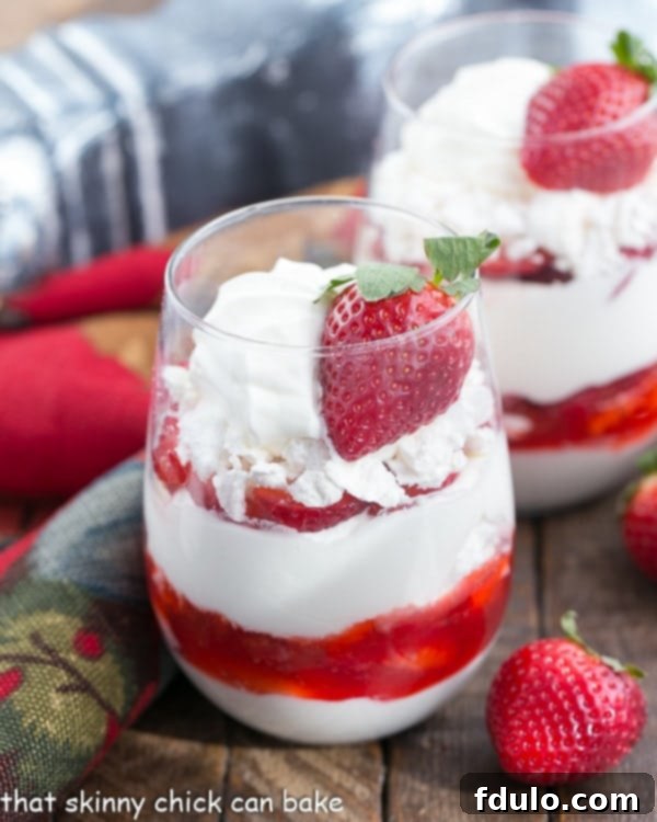 Fruit parfait with layers of whipped cream, crushed meringue cookies and sliced strawberries in parfait glasses with fresh strawberries nearby
