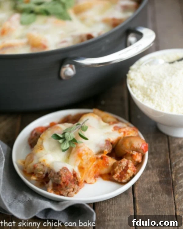 A white dinner plate piled high with Cavatini Supreme, featuring melted cheese and visible pasta, with the full casserole pan blurred in the background, suggesting a generous portion.