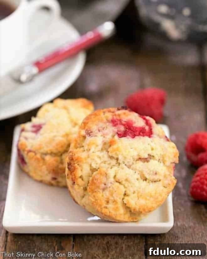 Freshly baked Raspberry Cream Scones on a pristine square white plate, ready to be enjoyed. Each scone is golden brown and studded with red raspberries.