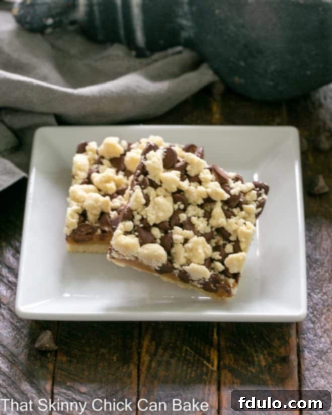 Two golden-brown chocolate caramel bars with streusel topping on a square white plate, ready to be enjoyed.