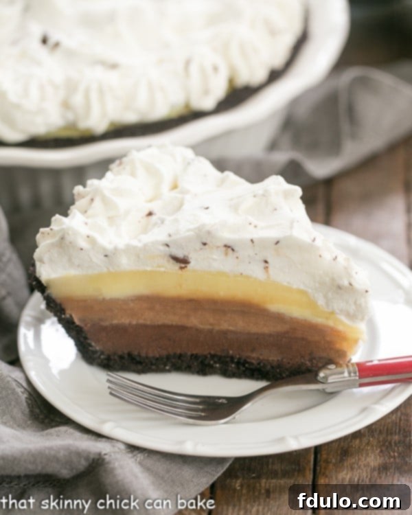 A perfectly sliced Triple Chocolate Layer Pie Recipe revealing its distinct layers of dark, milk, and white chocolate custard, topped with a generous swirl of whipped cream, on a pristine white dessert plate.
