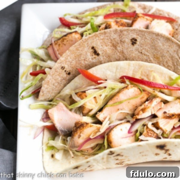 Best Fish Tacos Recipe with Mango Salsa - Roasted salmon with all the fixings for a sophisticated seafood taco An overhead view of the Best Fish Tacos Recipe, featuring three loaded Salmon Tacos with Mango Salsa, presented on a square ceramic plate, ready to be enjoyed.