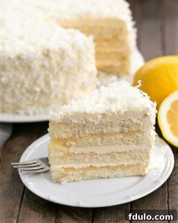 A perfectly sliced piece of Lemon Layer Cake with Lemon Curd Filling on a pristine white dessert plate, showcasing its four luscious layers and creamy frosting.