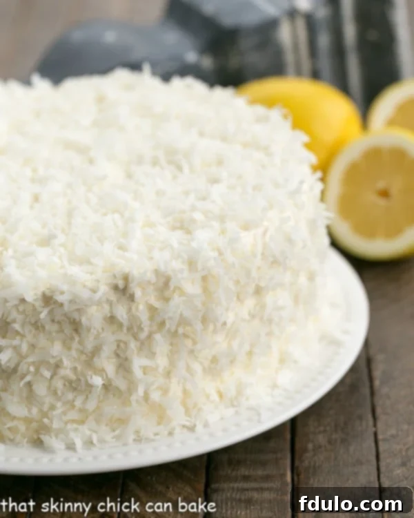 A stunning Lemon Layer Cake with Lemon Curd Filling, artfully frosted with Lemon Swiss Meringue Buttercream and delicately adorned with coconut flakes, presented on a white serving plate.