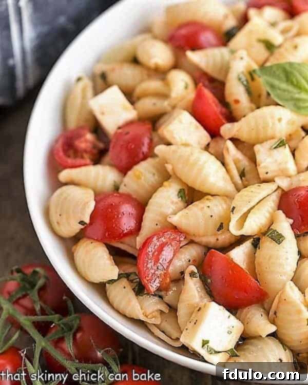 A close-up view of Tomato Basil Pasta Salad with Mozzarella & Fontina, highlighting the texture of the pasta, the freshness of the herbs, and the creamy cheese cubes.