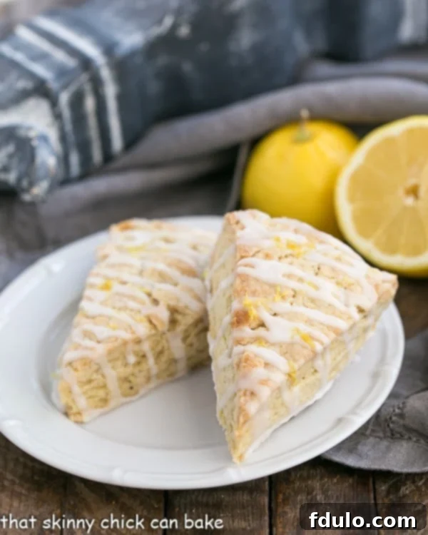 Two Glazed Lemon Tea Scones on a white plate with fresh lemons in the background, highlighting their delightful citrus infusion.
