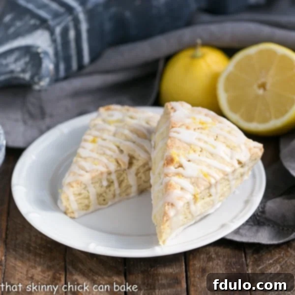 Two Glazed Lemon Tea Scones displayed on a pristine white round plate, showcasing their inviting texture and delicious glaze.