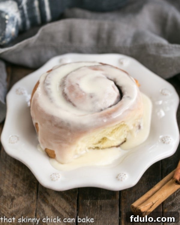 A close-up view of a perfectly glazed homemade cinnamon bun on an elegant white plate, ready to be enjoyed.