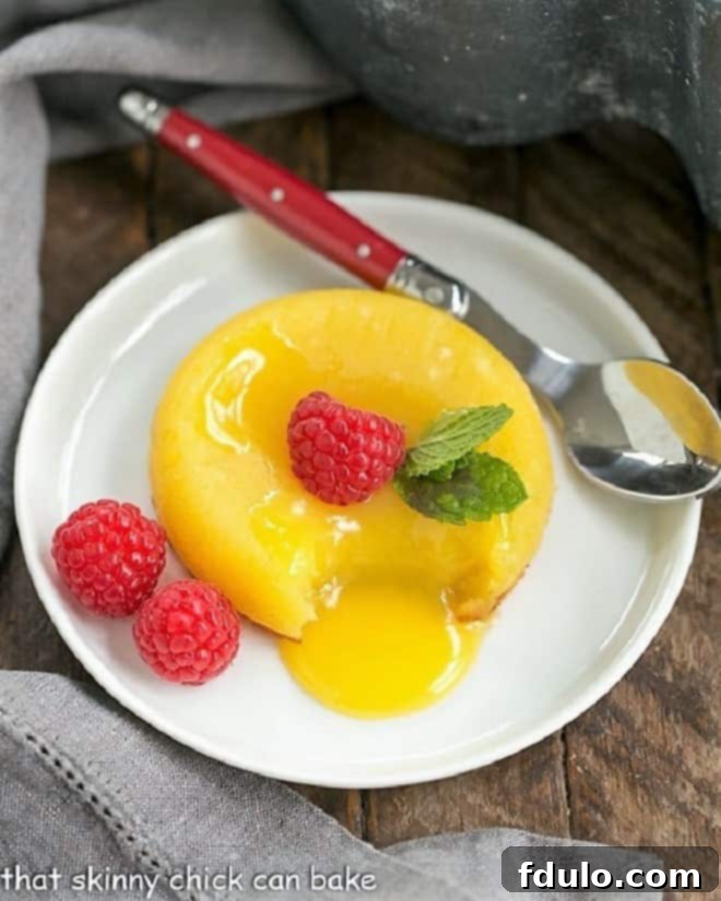 White Chocolate Molten Lava Cakes - Dreamy individual white chocolate cakes with molten centers! Two White Chocolate Molten Lava Cakes on a white plate with a red handled spoon, showcasing their soft, gooey centers.