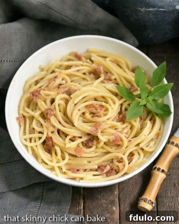 Spaghetti Carbonara - Pasta combined with grated cheese, eggs and pancetta create a simple, delectable entree Overhead view of a bowl of spaghetti carbonara with a basil sprig garnish. A true classic of Italian cuisine.