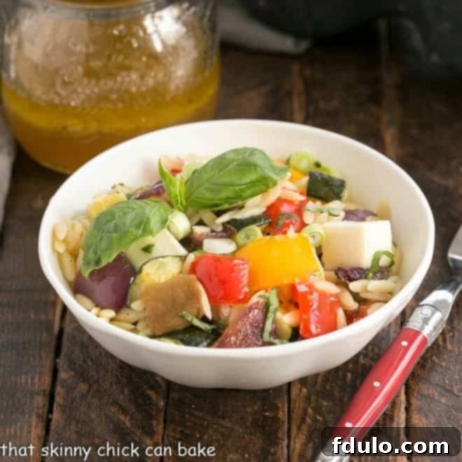 A small white bowl filled with roasted vegetable orzo pasta salad, garnished with fresh basil.