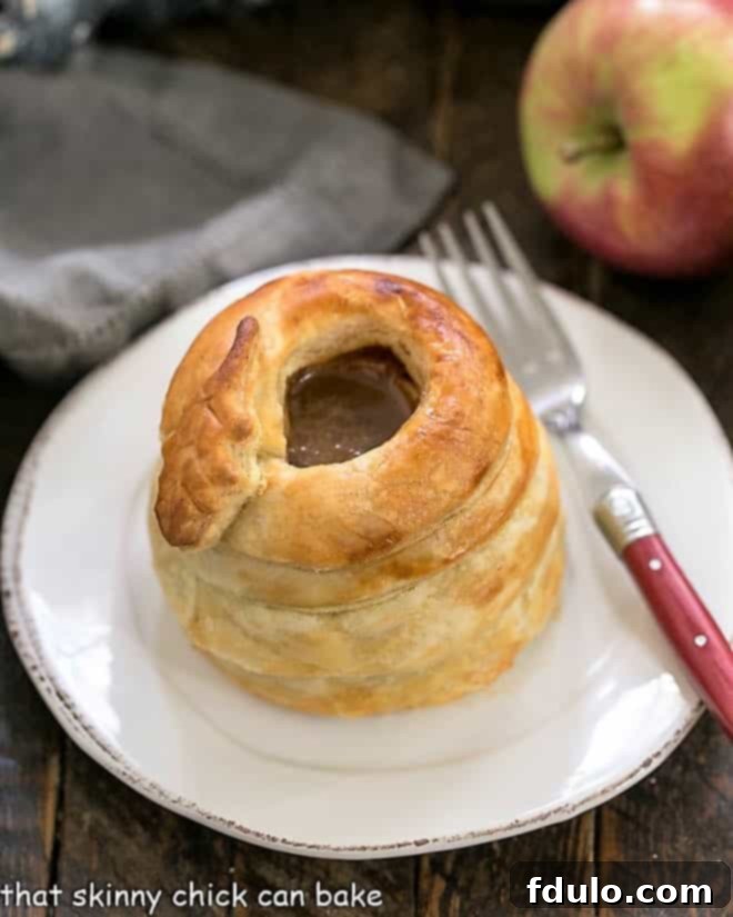 Pastry Wrapped Baked Caramel Apples are an elegant, delicious autumn dessert recipe! A single beautifully baked pastry-wrapped caramel apple presented on a pristine white round plate, showcasing its golden, flaky crust.
