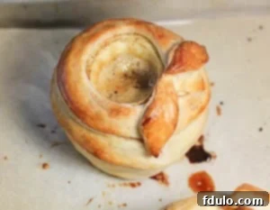 Caramel apples en Croute AKA baked apples wrapped in pasty and filled with caramel sauce Three golden pastry-wrapped caramel apples arranged on a parchment-lined baking sheet, glistening after being freshly baked.