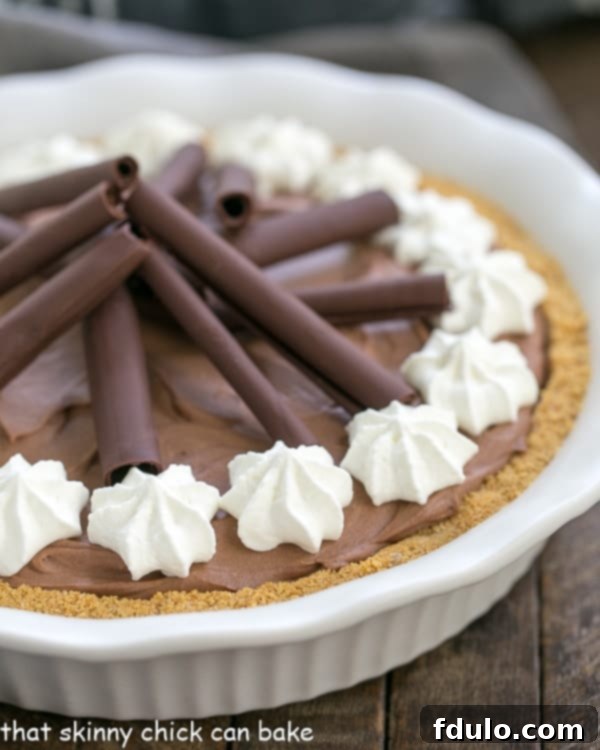 A perfectly sliced chocolate cream pie in a white ceramic pie plate, revealing its creamy chocolate filling and graham cracker crust.