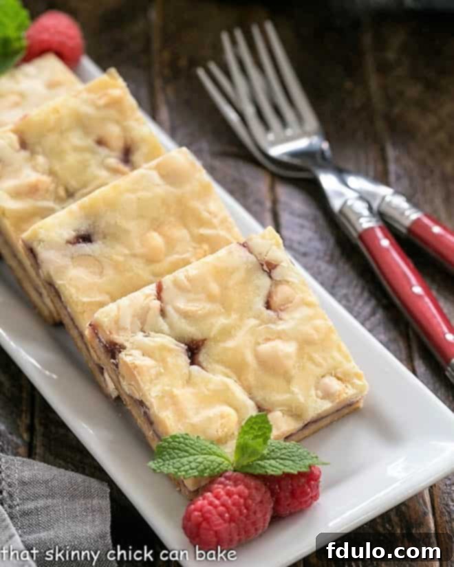 White chocolate raspberry bars on a white tray with raspberries and mint.