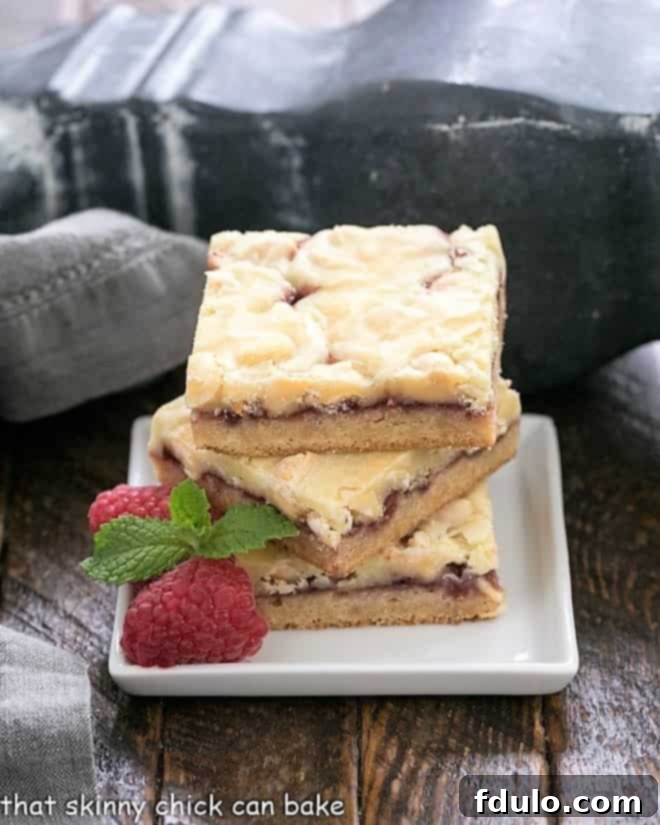 A stack of white chocolate raspberry bars on a square white plate with raspberries and mint to garnish.