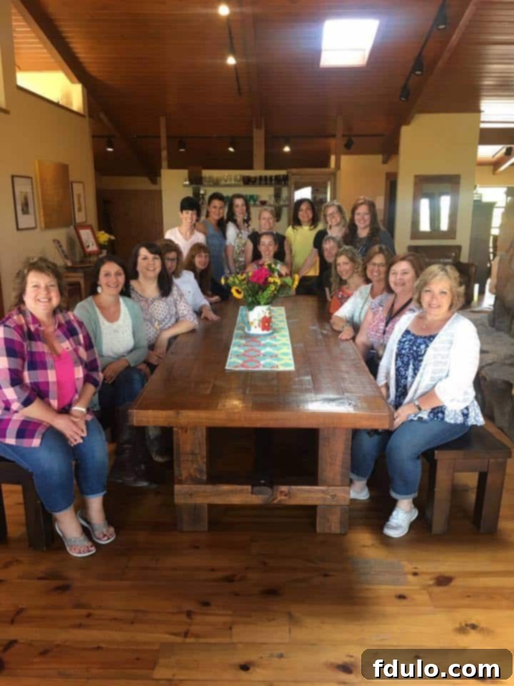 A jovial group of people seated around a rustic wooden table in the vibrant studio kitchen of the Pioneer Woman's Lodge, enjoying a meal and each other's company, a highlight of the trip.