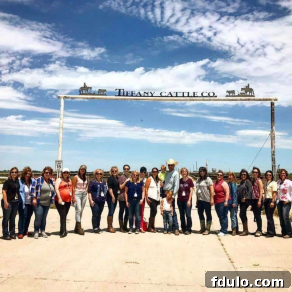 A group of smiling individuals, including the author, standing proudly in front of a ranch sign, bathed in the warm sunlight of a gorgeous day, ready to explore a feedlot and learn about beef production.