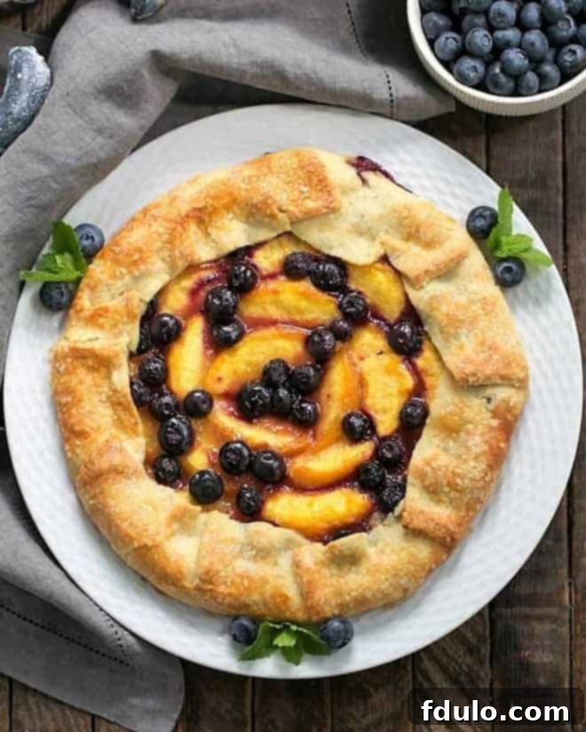 Rustic Peach Blueberry Galette 2 An inviting overhead view of a freshly baked Peach Blueberry Galette, beautifully arranged on a white serving plate and garnished with sprigs of fresh mint and extra blueberries, highlighting its rustic appeal.