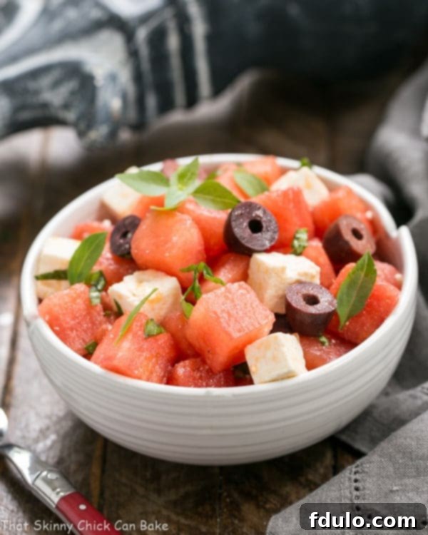 A close-up view of Watermelon Feta Basil Salad with Balsamic Vinaigrette in a white ceramic bowl, accompanied by a red-handled fork.