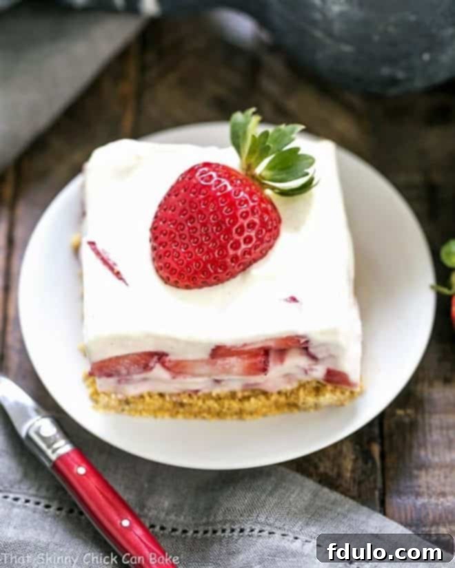 A perfectly portioned slice of Strawberry Cheesecake Lush Dessert, showing the distinct layers of crust, creamy filling, and fresh strawberry topping on a round white plate.