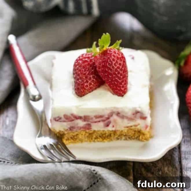 A close-up of a Strawberry Cheesecake Lush Dessert slice, showcasing the creamy texture of the filling and the vibrant red strawberries, served on a elegant white dessert plate.