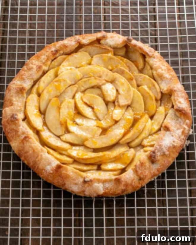 A freshly baked apple galette cooling on a wire rack, with a pastry brush poised to apply a glistening jam glaze to the apples.