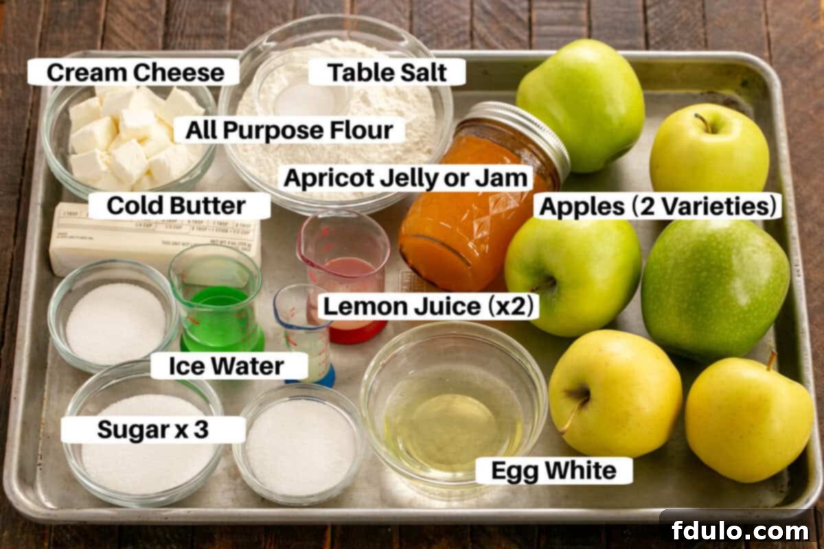 A baking sheet displaying all the fresh ingredients laid out for making an Apple Galette, including sliced apples, butter, cream cheese, flour, sugar, and cinnamon.