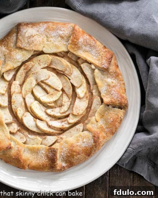 A close-up, partial overhead view of a baked Apple Tart on a white serving plate, highlighting the textured crust and the sweet apple filling.