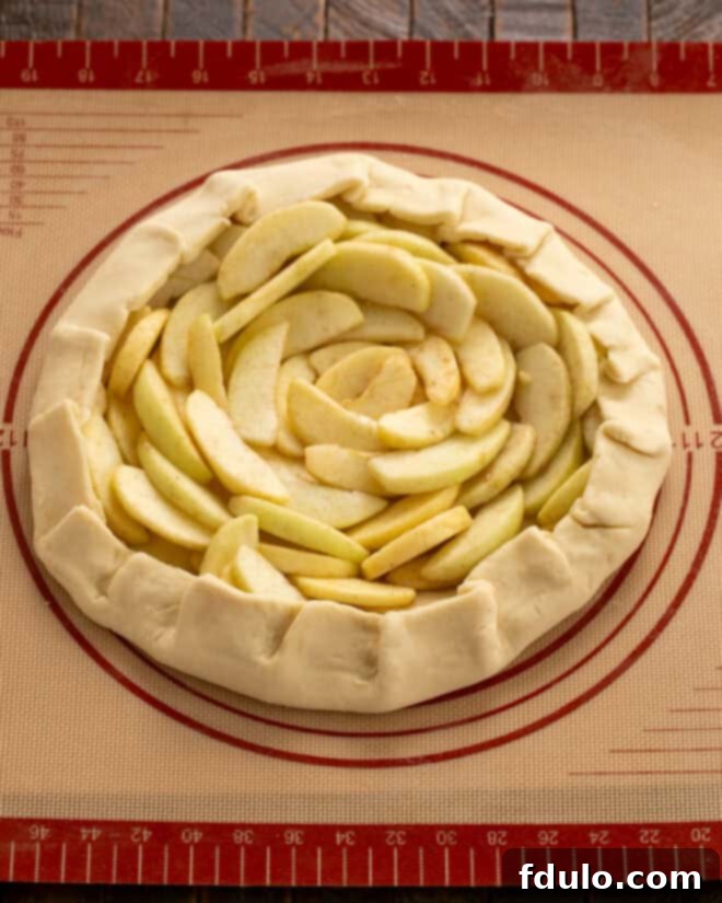 An unbaked apple galette on a baking sheet, with apple slices beautifully arranged on the crust and the dough edges gently folded over to contain the filling.