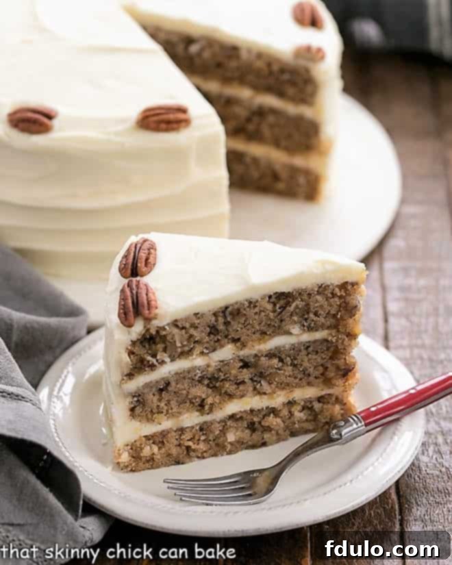 Hummingbird Cake with Coconut - A dense, banana cake chock full of pecans, coconut and pineapple and slathered in cream cheese frosting! Hummingbird Cake with Coconut slice on a white dessert plate with the whole cake in the background.
