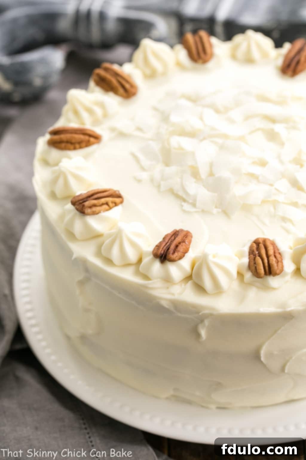Classic Hummingbird Cake with Coconut - A dense, banana cake chock full of pecans, coconut and pineapple and slathered in cream cheese frosting! Classic Hummingbird Cake with Coconut on a white serving plate.