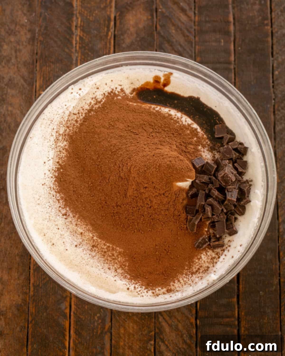 Cocoa powder, chopped chocolate, and balsamic vinegar being added to the beaten egg whites.