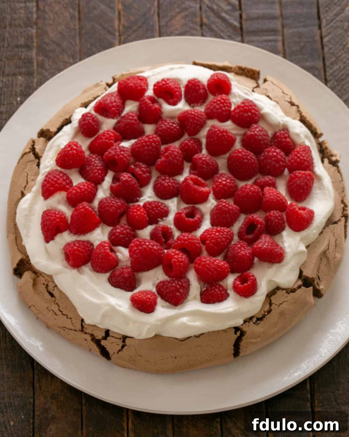 Chocolate Raspberry Pavlova cooled and topped generously with whipped cream and fresh raspberries, with chocolate shavings.