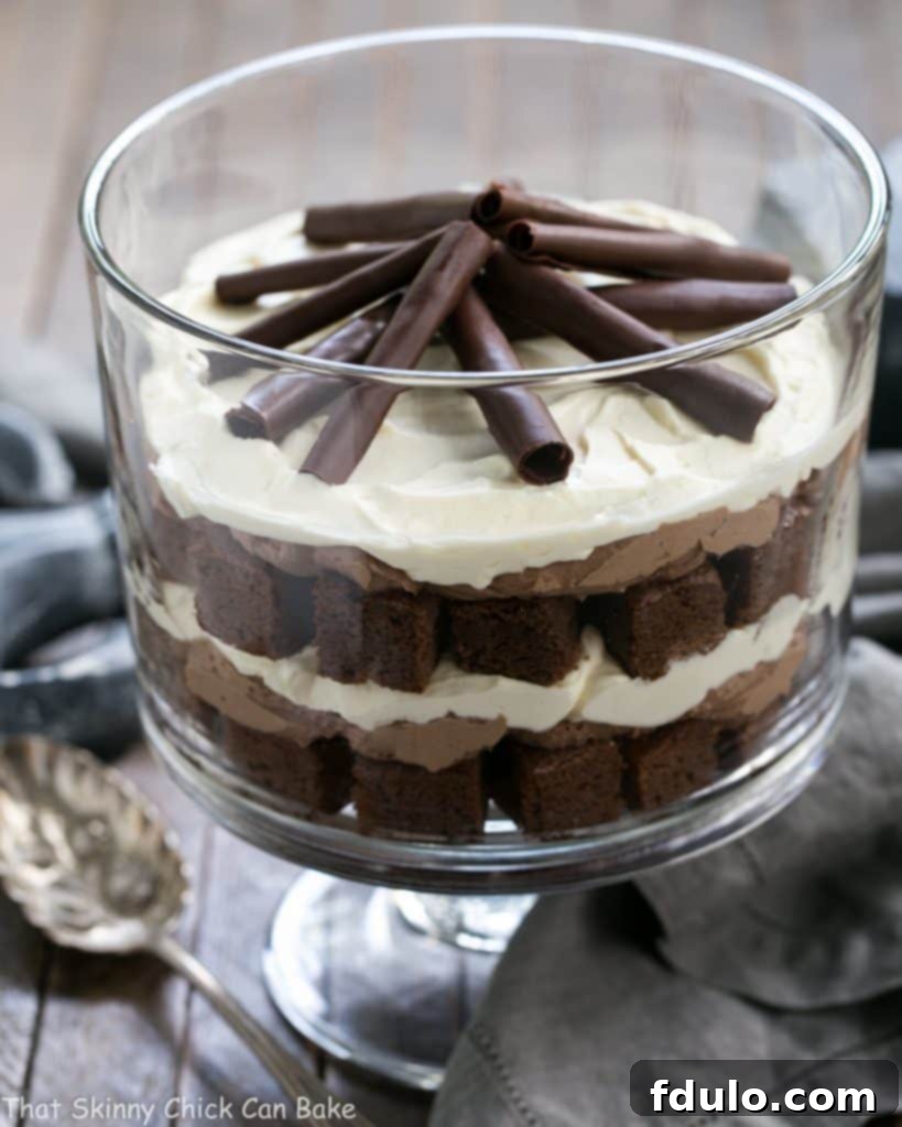 Fudgy Brownie Trifle with Chocolate Mousse - 3 outrageously delicious layers plus chocolate curls! A stunning Fudgy Brownie Trifle with layers of chocolate mousse and fluffy cream, elegantly presented in a glass trifle dish with a silver serving spoon ready for guests.