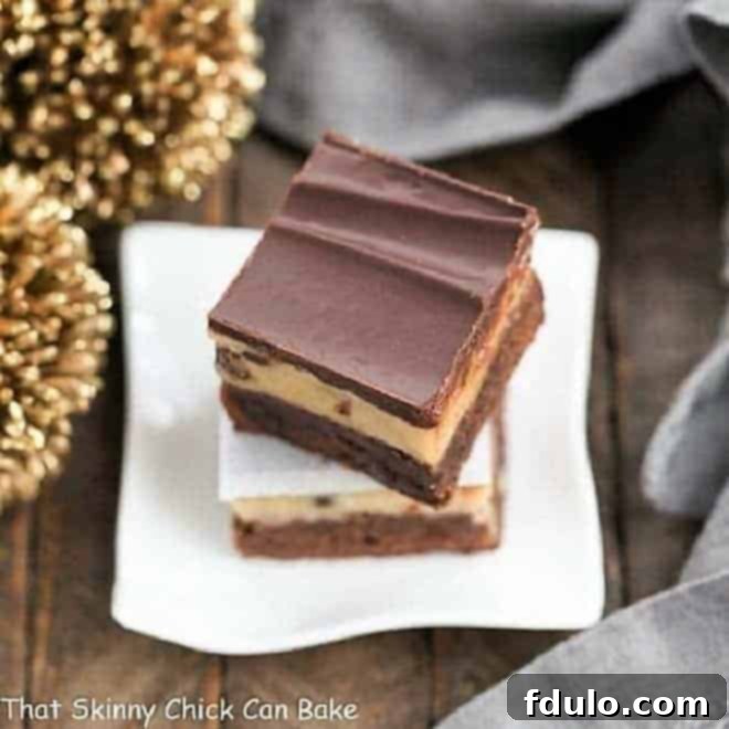 Close-up stack of three Chocolate Chip Cookie Dough Brownies on a small white plate, highlighting the distinct layers of brownie, cookie dough, and ganache.