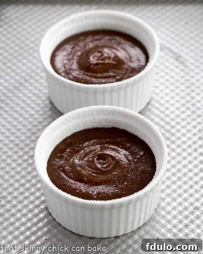 Close-up of rich chocolate lava cake batter perfectly portioned into four buttered and sugared ramekins, ready for baking.