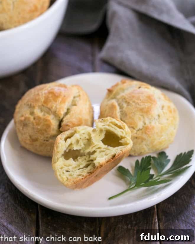 Close-up of baked cheese puffs on a white plate, with one broken open to show its hollow, airy interior.