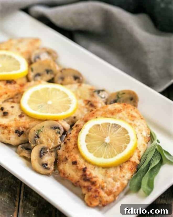 Creamy Chicken Marsala with Herbed Mushrooms on a white ceramic serving dish with lemons, mushrooms and sage.