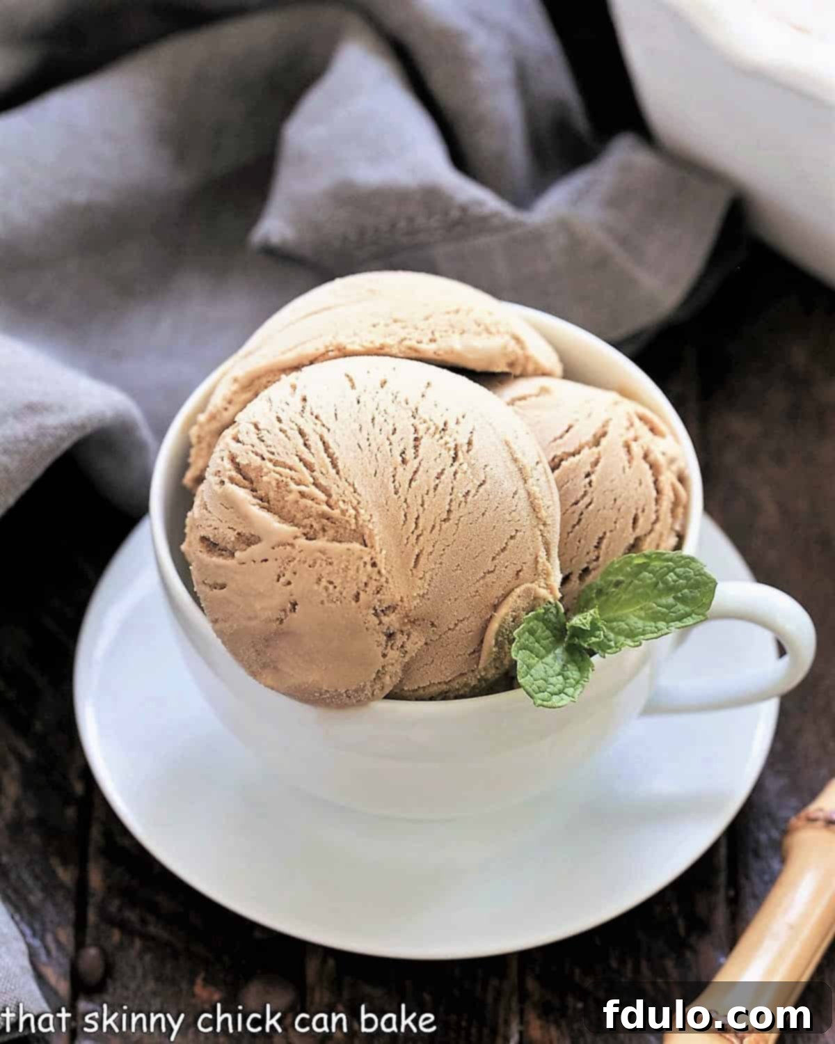 Two scoops of homemade coffee ice cream in a white coffee cup, garnished with a sprig of fresh mint.